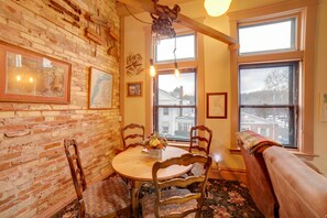 A dining area with a brick wall, wooden chairs, a round table, and a window with a view of a building.