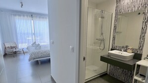 Quarto de hotel moderno com uma cama grande, banheiro separado com chuveiro de vidro e varanda com vista.