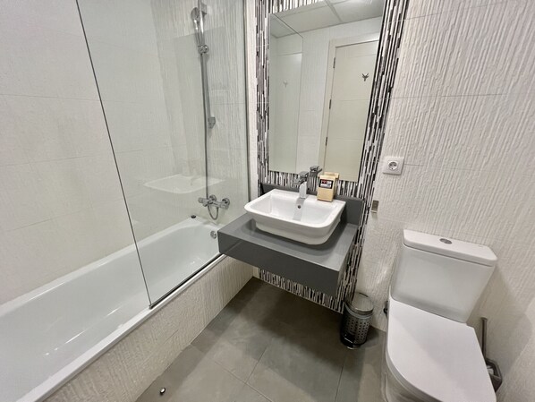 A modern bathroom with a glass-enclosed shower, a white sink, and a toilet.