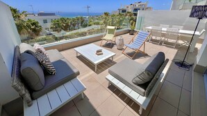 Terraço no telhado com um sofá, uma mesa e uma cadeira, com vista para a paisagem urbana e o mar.