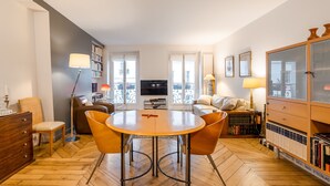 A living room with a round wooden table, two orange chairs, a sofa, a TV, and a bookshelf. - Pompidou Hideaway, by Veeve (Paris)