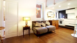 A modern kitchen with a built-in oven, a dining area with a white table and chairs, and a cozy seating area with a sofa and a lamp.