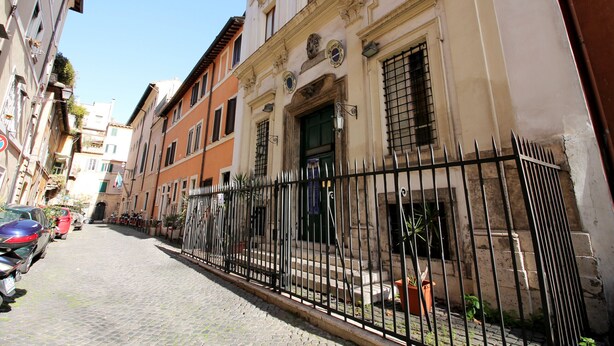 A cobblestone street lined with historic buildings, a black metal fence, and parked cars.