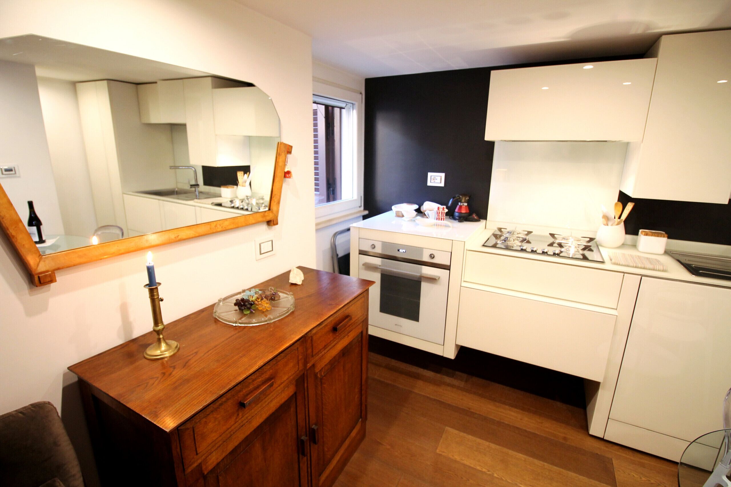 A modern kitchen with white cabinets, a wooden countertop, a stove, an oven, and a large mirror.