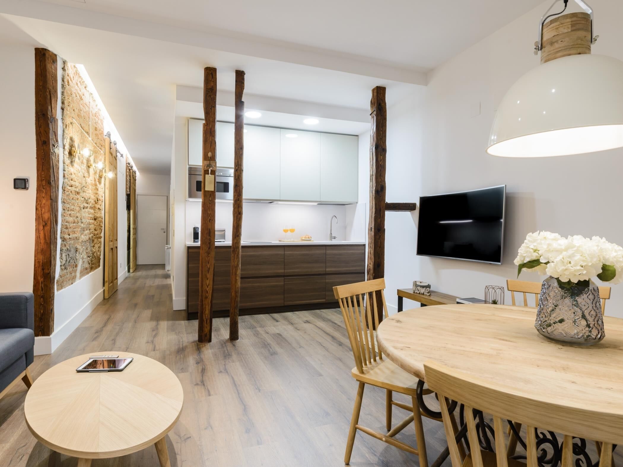 A modern kitchen with wooden accents, a dining area with a round table and chairs, and a flat-screen TV mounted on the wall.