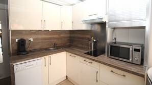 A compact kitchen with white cabinets, a dishwasher, a microwave, and a built-in oven. - Maisonette T2  et parking dans résidence avec piscine (Canet-en-Roussillon)