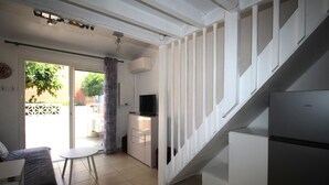 A compact living space with a staircase, a television, a small table, and a sofa. - Maisonette T2  et parking dans résidence avec piscine (Canet-en-Roussillon)