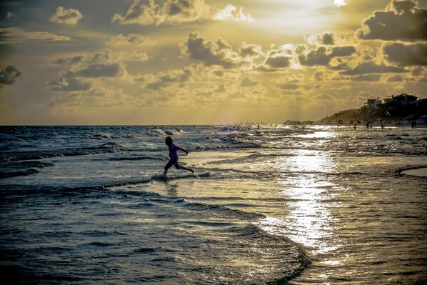 A beach scene with waves, a person running, and buildings in the background. - WaterColor Beach Home w/ Resort Amenity Passes, Sleeps 8 + Free Tickets! (Santa Rosa Beach)
