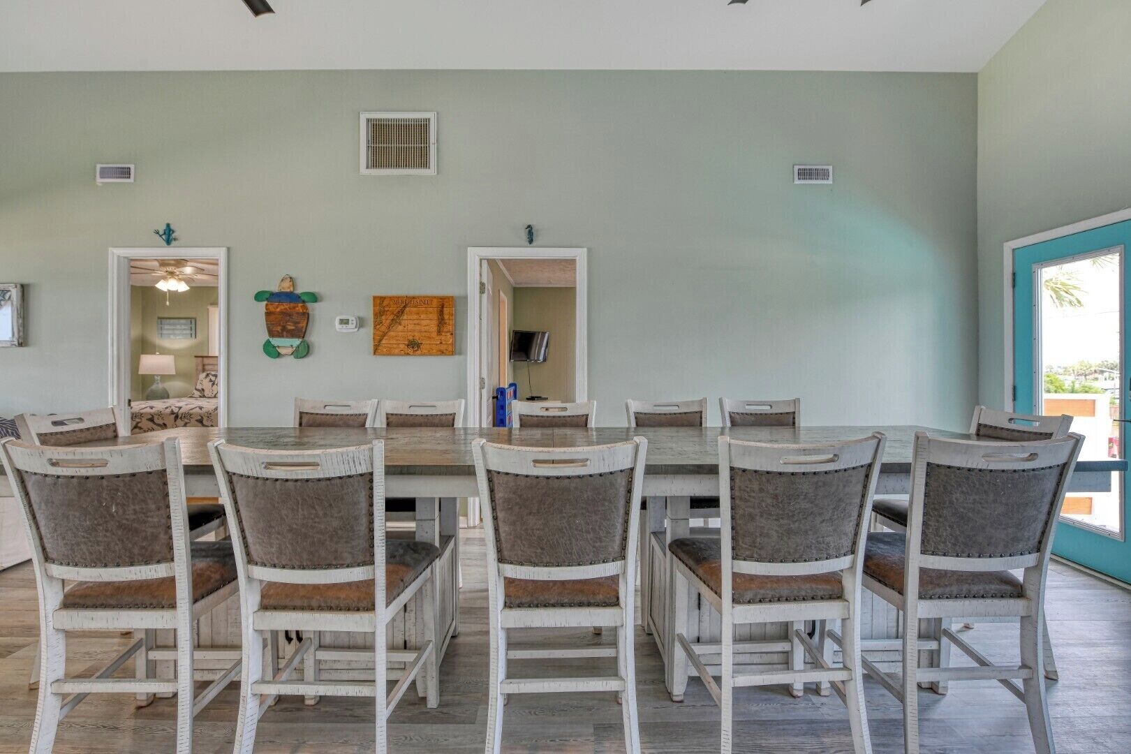 Un espace repas comprenant une grande table et six chaises, un téléviseur fixé au mur, et une porte donnant sur une autre pièce.