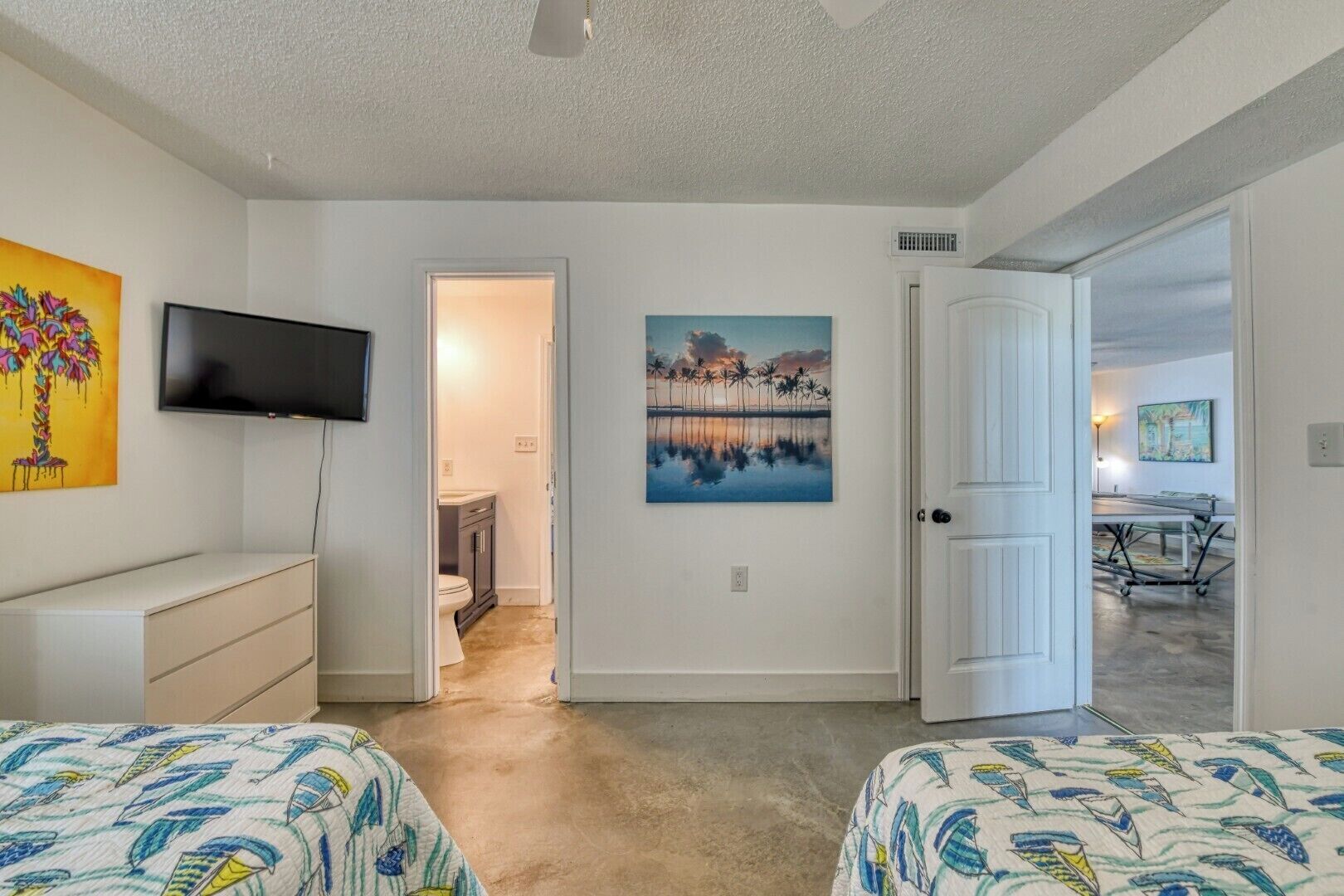 A bedroom with two beds, a TV, a painting, and a door leading to another room.