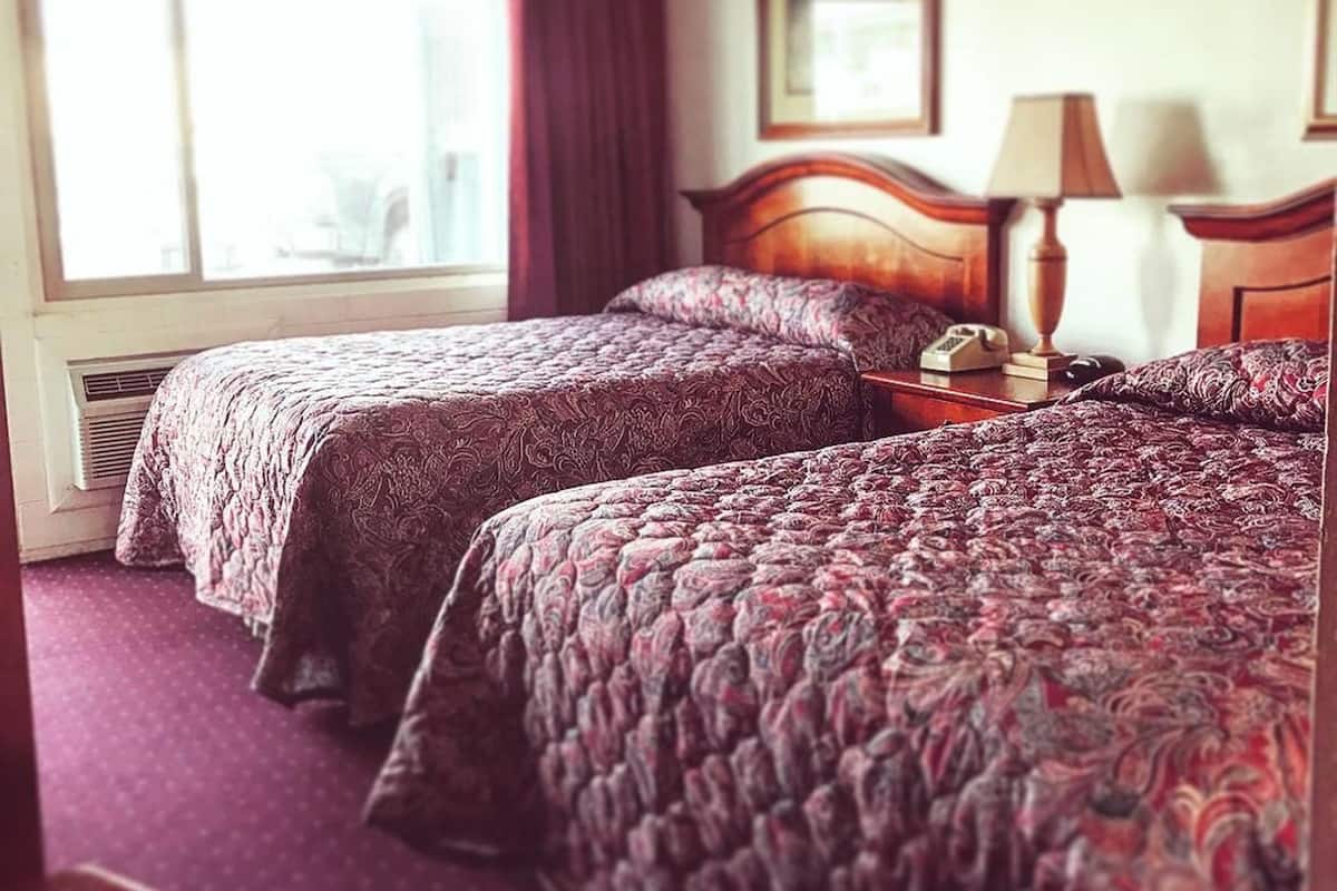 A hotel room with two beds, a window, a lamp, and a framed picture on the wall.