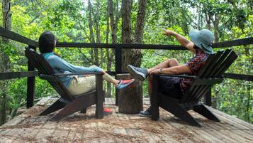 Two people sitting on wooden benches in a forested area with a wooden deck.