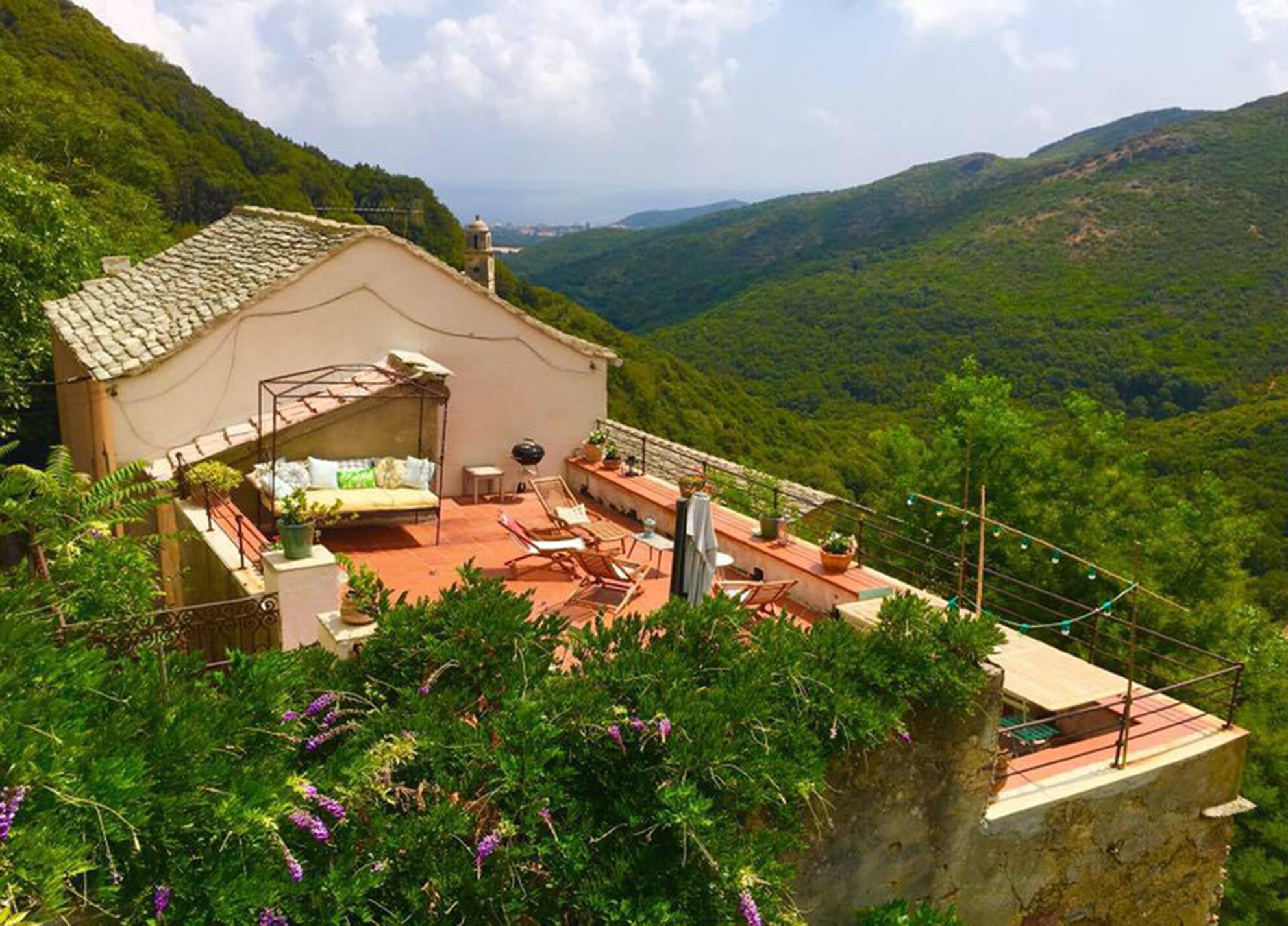 Une villa de style rustique, dotée d’un toit en tuiles de terre cuite, d’un espace extérieur aménagé et couvert, et offrant une vue imprenable sur un paysage montagneux.