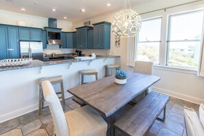 A modern kitchen with teal cabinets, a stainless steel range hood, and a large island with bar stools.