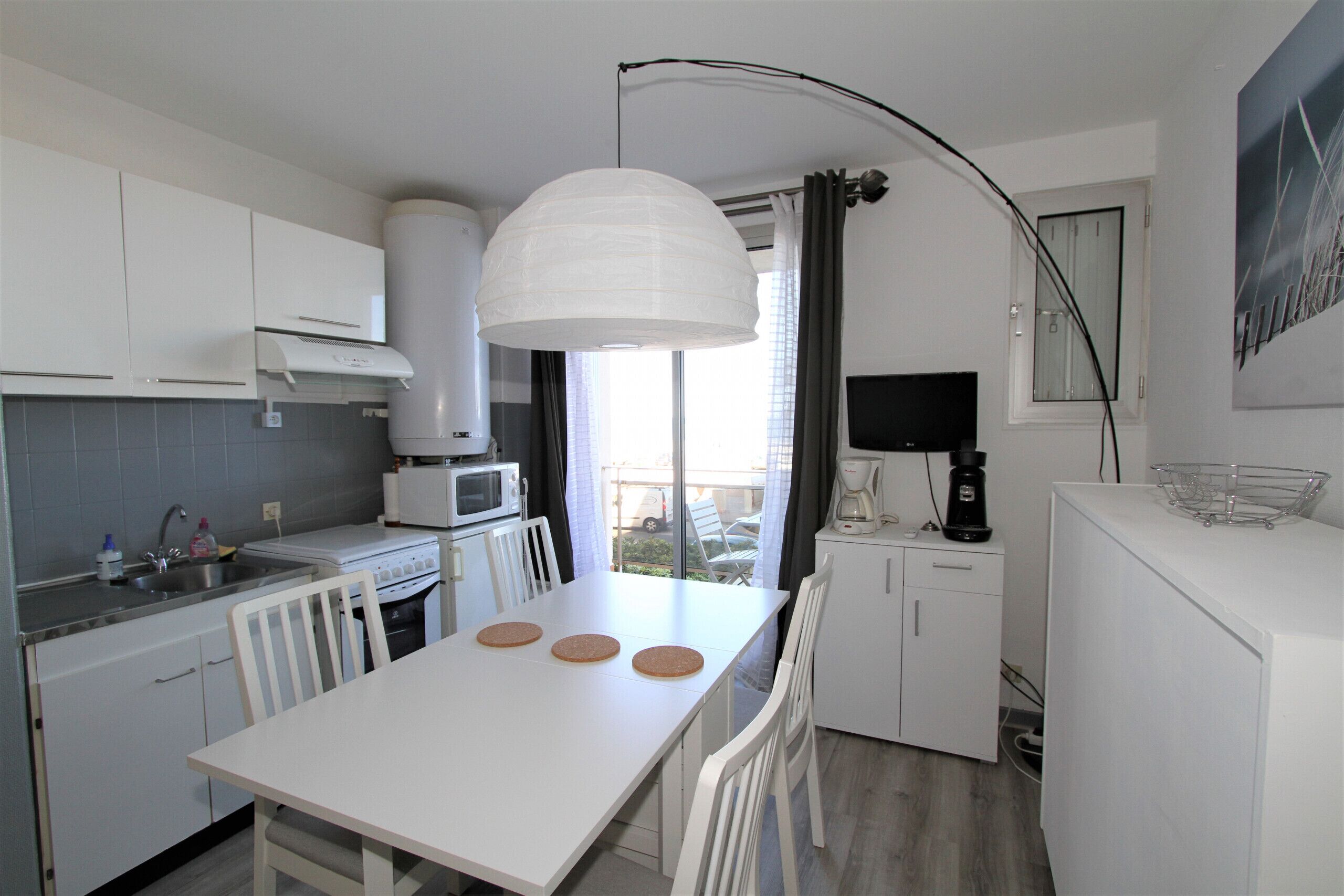 Una cocina moderna con armarios blancos, una mesa de comedor con sillas, una cafetera y un ventanal con cortinas.
