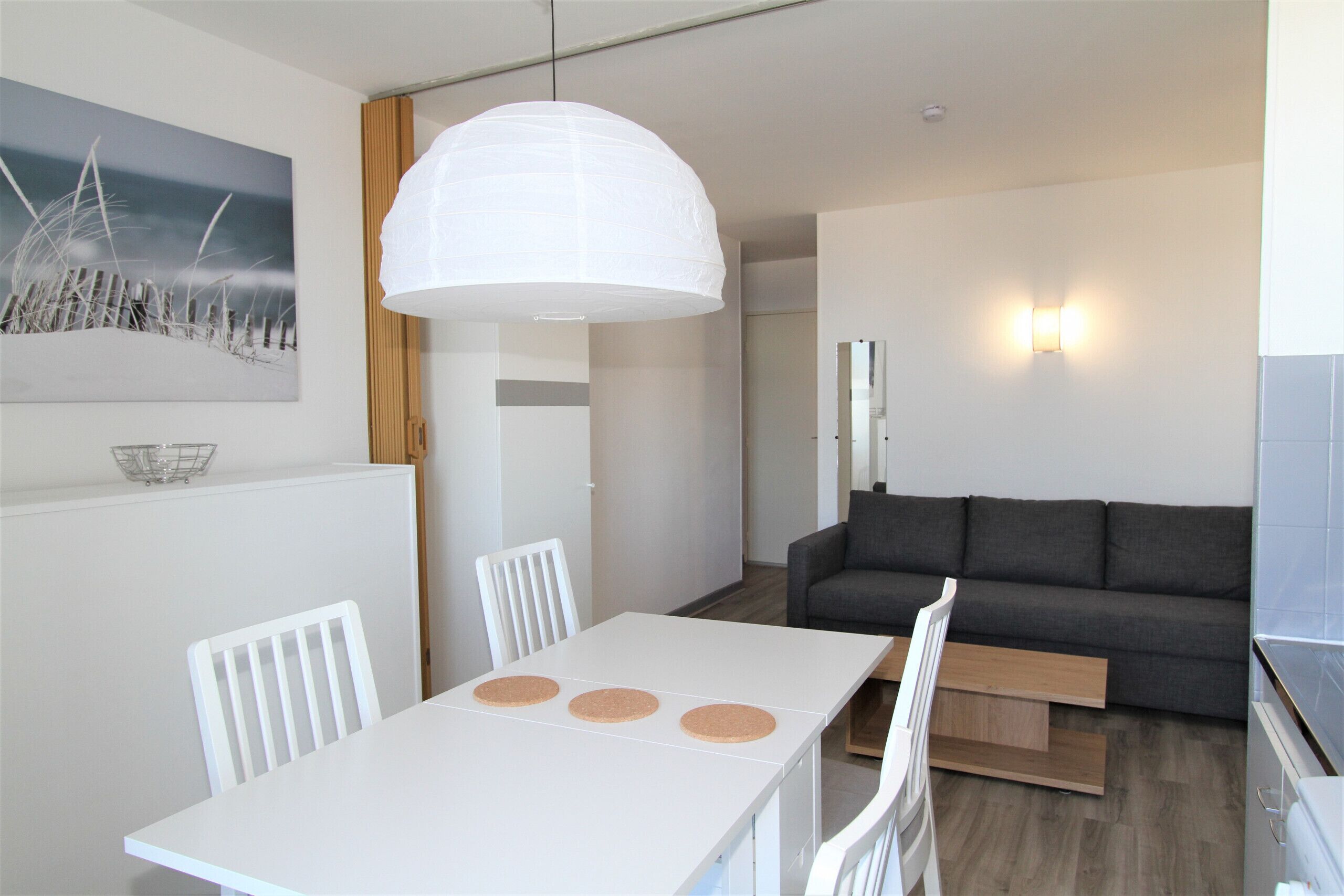 Un salon moderne avec une table à manger blanche, un canapé gris et un grand luminaire suspendu blanc.