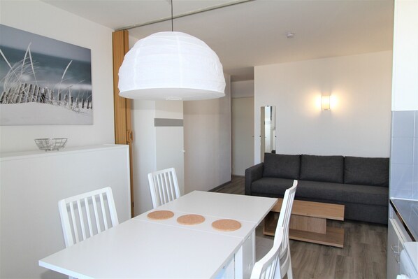 Un salon moderne avec une table à manger blanche, un canapé gris et un grand luminaire suspendu blanc.