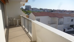 A balcony with a tiled floor, white railings, and a view of neighboring buildings.