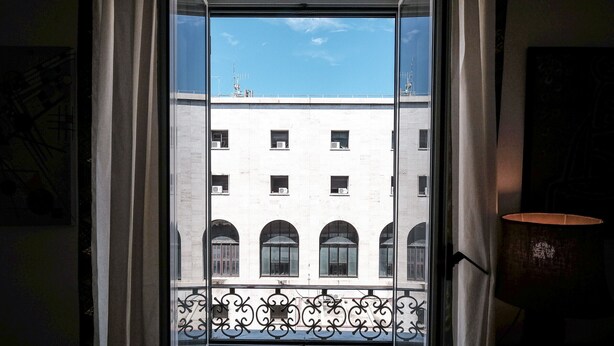 A view through a window with a balcony railing, a building with multiple windows, and a clear sky. - Casa Linda (Roma)
