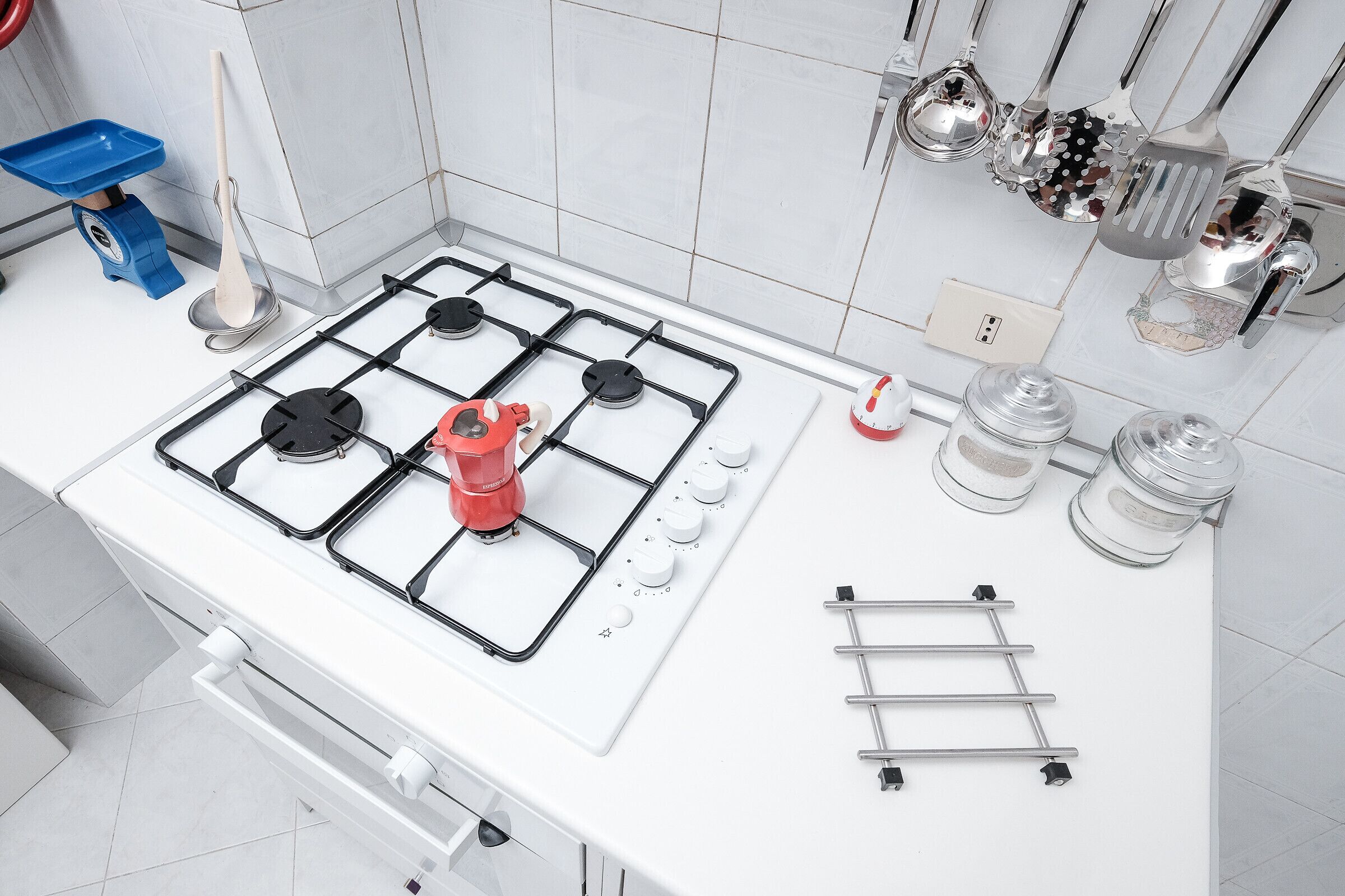 Una cocina con una estufa blanca, un hervidor rojo y varios utensilios colgados en la pared.