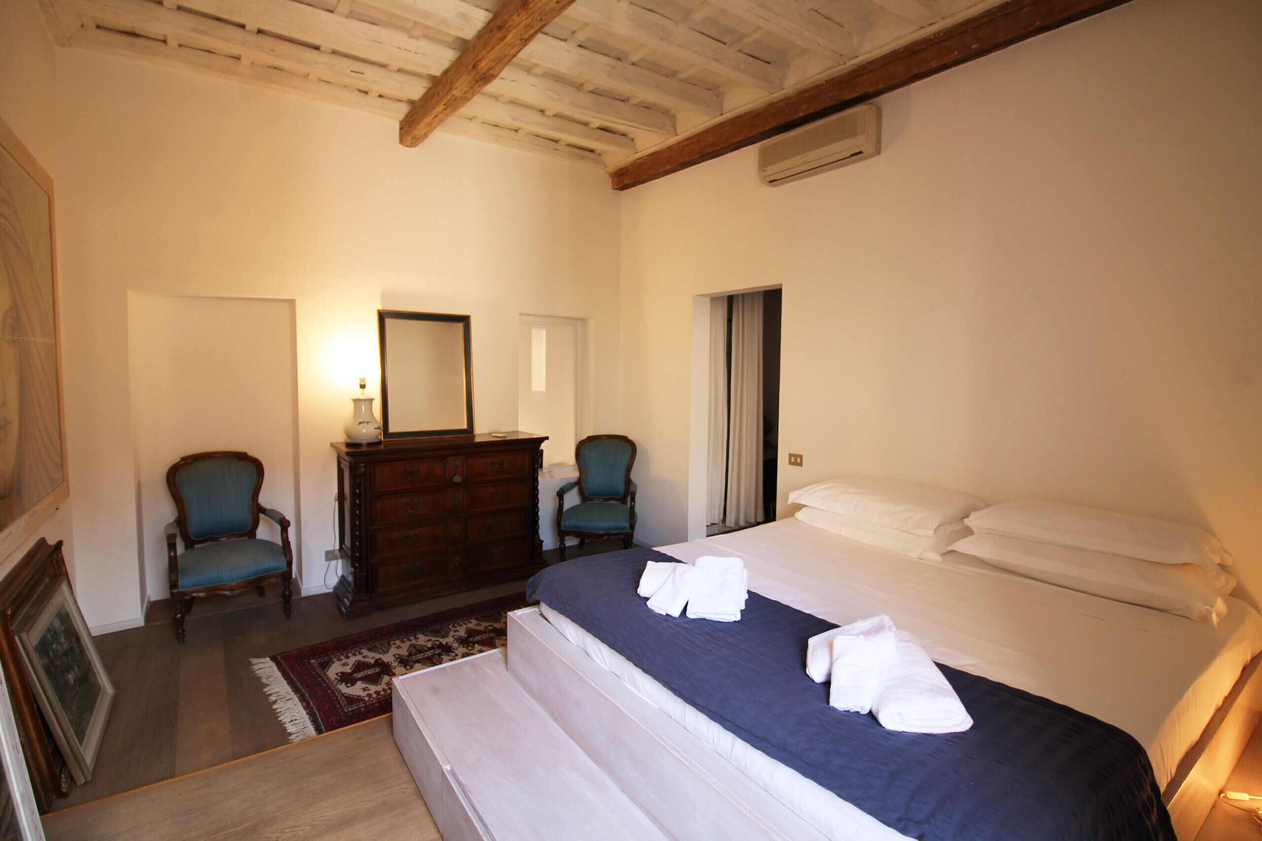 Un dormitorio con una cama grande, dos sillones, un aparador y un espejo.