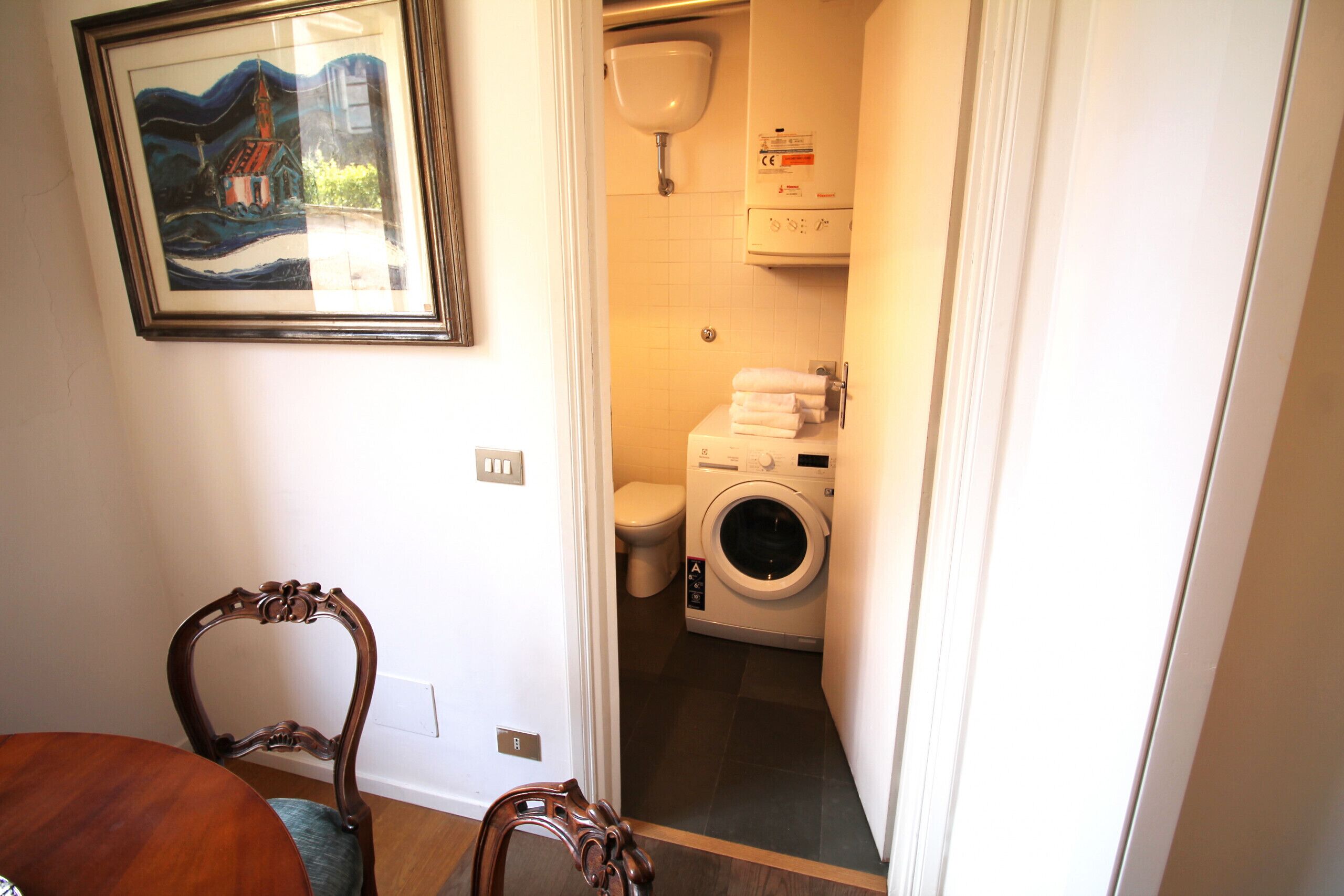A compact bathroom with a toilet, washing machine, and a framed picture on the wall.