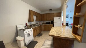 Cocina compacta con estufa, microondas y refrigerador. Cuenta con gabinetes de madera y encimera de granito.