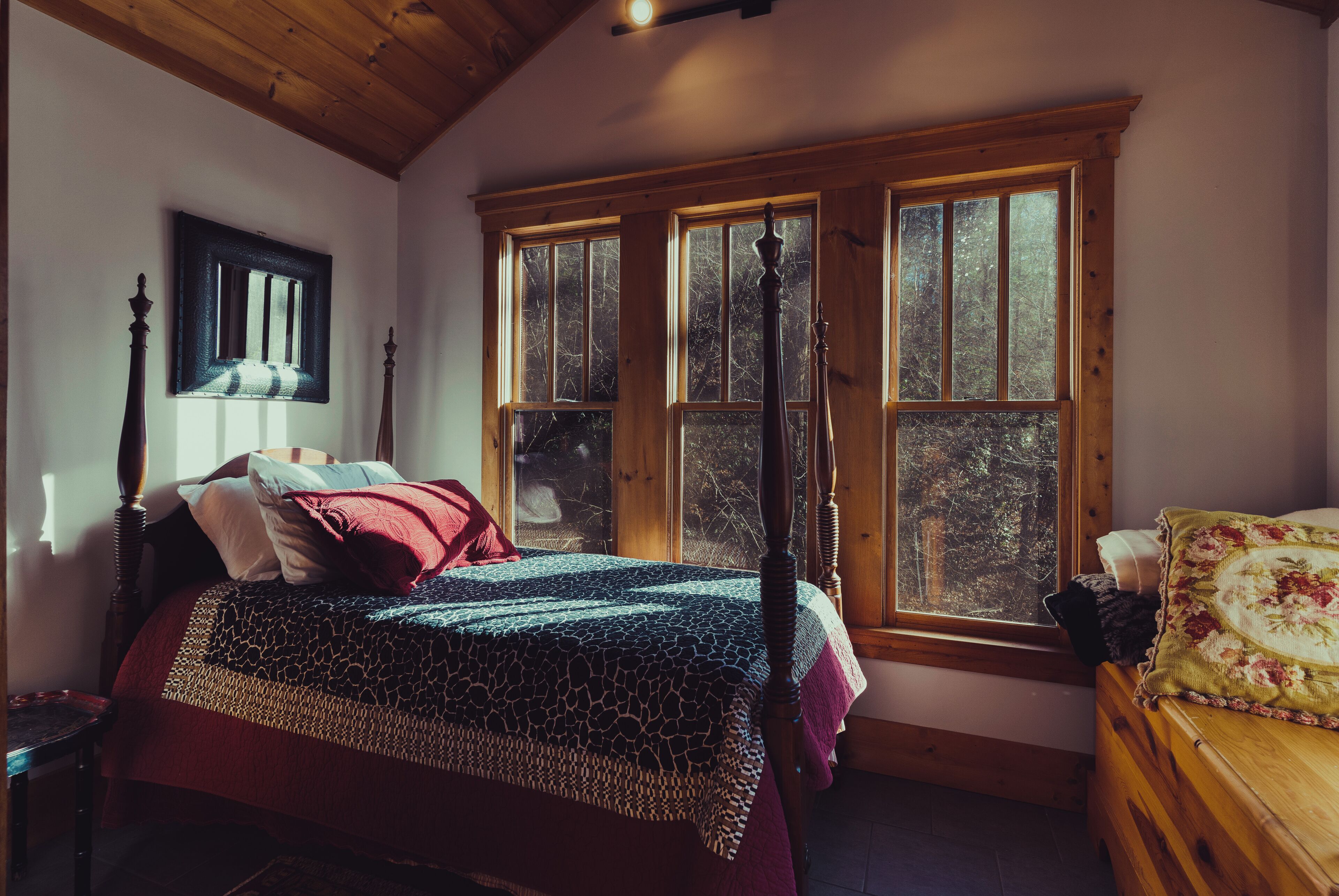 A bedroom with a large bed, a wooden headboard, a window with a view of trees, and a wooden ceiling.