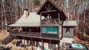 A two-story cabin with a balcony, surrounded by trees.