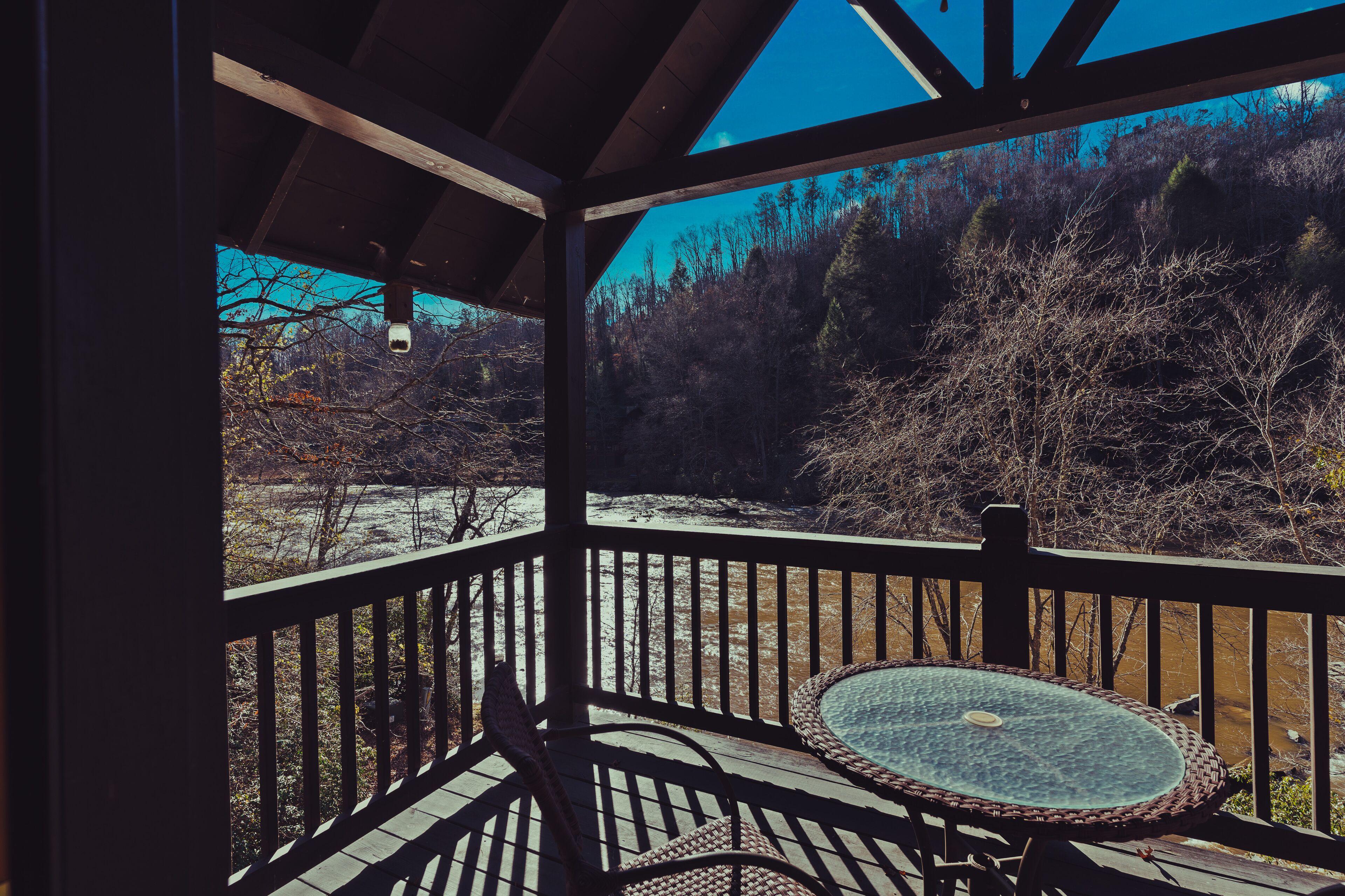 Un espace extérieur abrité, doté d’une table et de chaises, qui offre une vue sur un paysage naturel avec des arbres et une étendue d’eau.