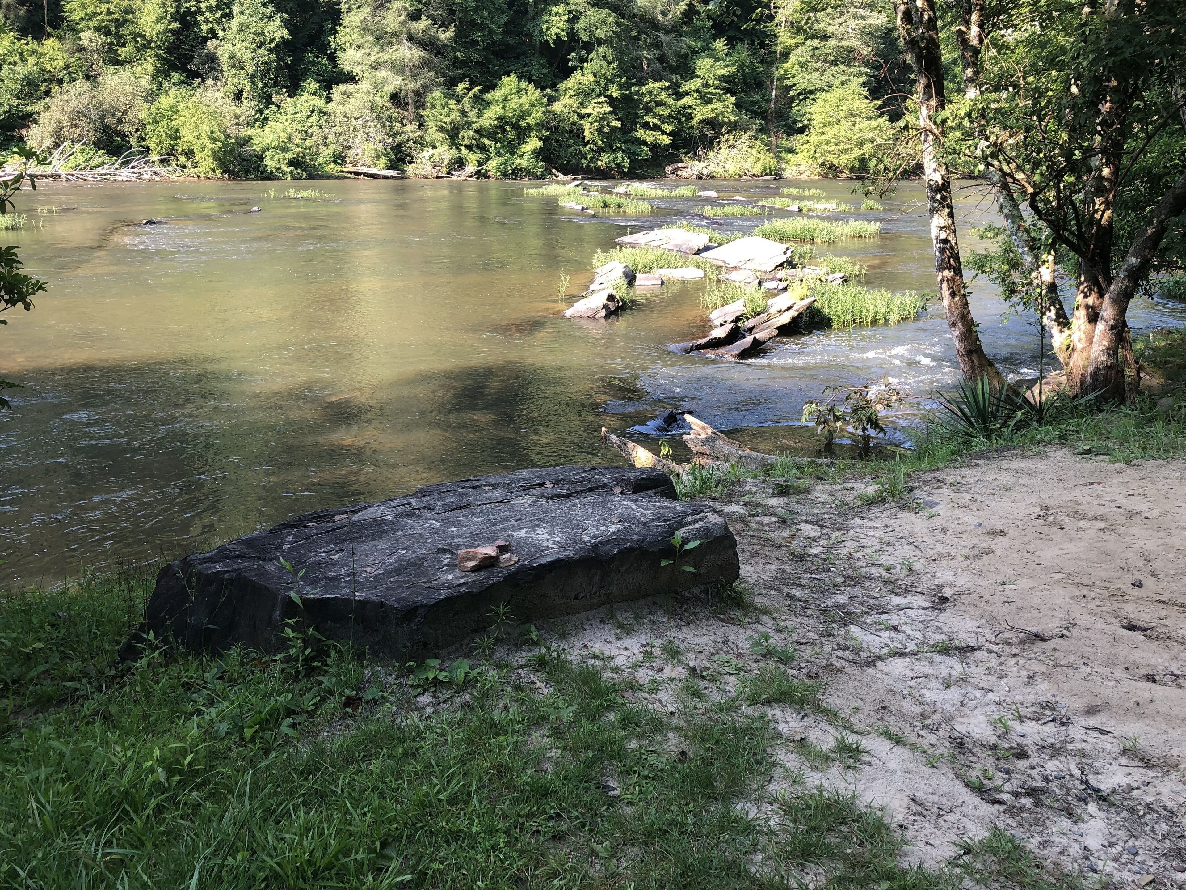 A natural landscape with a river, rocks, and trees.