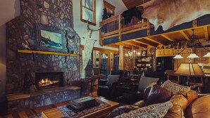 A rustic interior with a stone fireplace, leather furniture, and a chandelier.