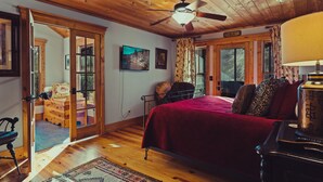 A bedroom with a wooden ceiling, a bed with a red blanket, a wooden dresser, and a chair.