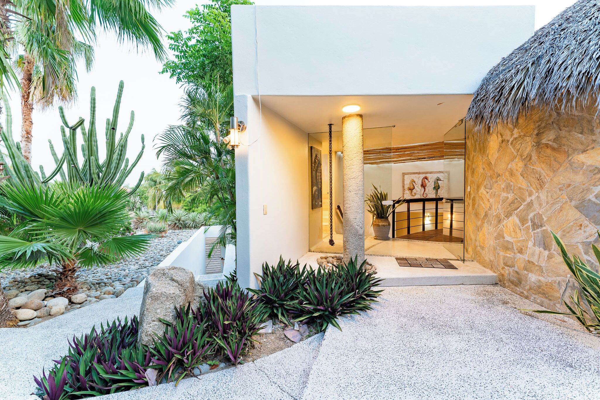 A modern building with a stone exterior, a thatched roof, and a well-maintained garden with cacti and ferns.