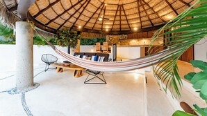 A hammock under a thatched roof, a wooden bench, a chair, and a kitchen area with a counter and cabinets. - Stunning Open-Air Villa w/ Private Pool (Huatulco)