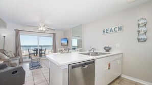 Une cuisine moderne équipée d’un lave-vaisselle, dotée d’un grand îlot central et offrant une vue sur la plage.