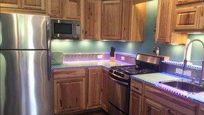 Una cocina completa con armarios de madera, electrodomésticos de acero inoxidable e iluminación debajo de los gabinetes.