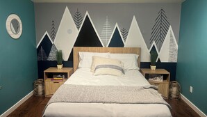 Un dormitorio con cama, dos mesitas de noche, un mural en la pared y un espejo circular.