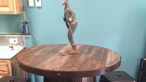 Una mesa redonda de madera con una escultura de venado de metal encima, rodeada por cuatro taburetes negros.