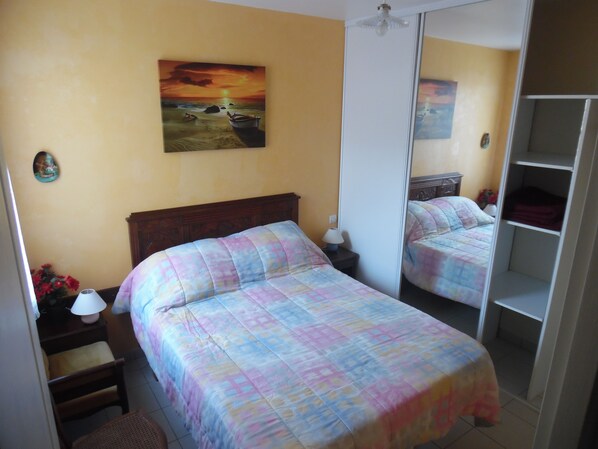 Une chambre à coucher avec un lit, une table de chevet, une lampe, un miroir et un tableau accroché au mur.