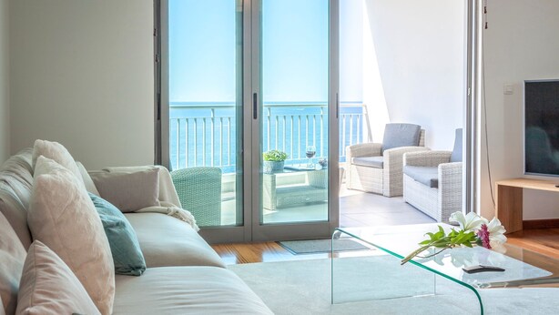 A modern living room with a sofa, a glass coffee table, and a TV on a wooden stand. - The Seaside Apartment by LovelyStay (Funchal)