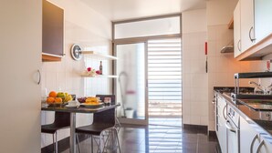 A compact kitchen with a dining area, a clock, and a view through a glass door. - The Seaside Apartment by LovelyStay (Funchal)