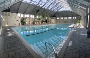 An indoor swimming pool with clear water, surrounded by lounge chairs and potted plants. - Pet &, Kid Friendly, Two FREE adult trikes (bikes)  PARKING NO WORRIES (Panama City Beach)