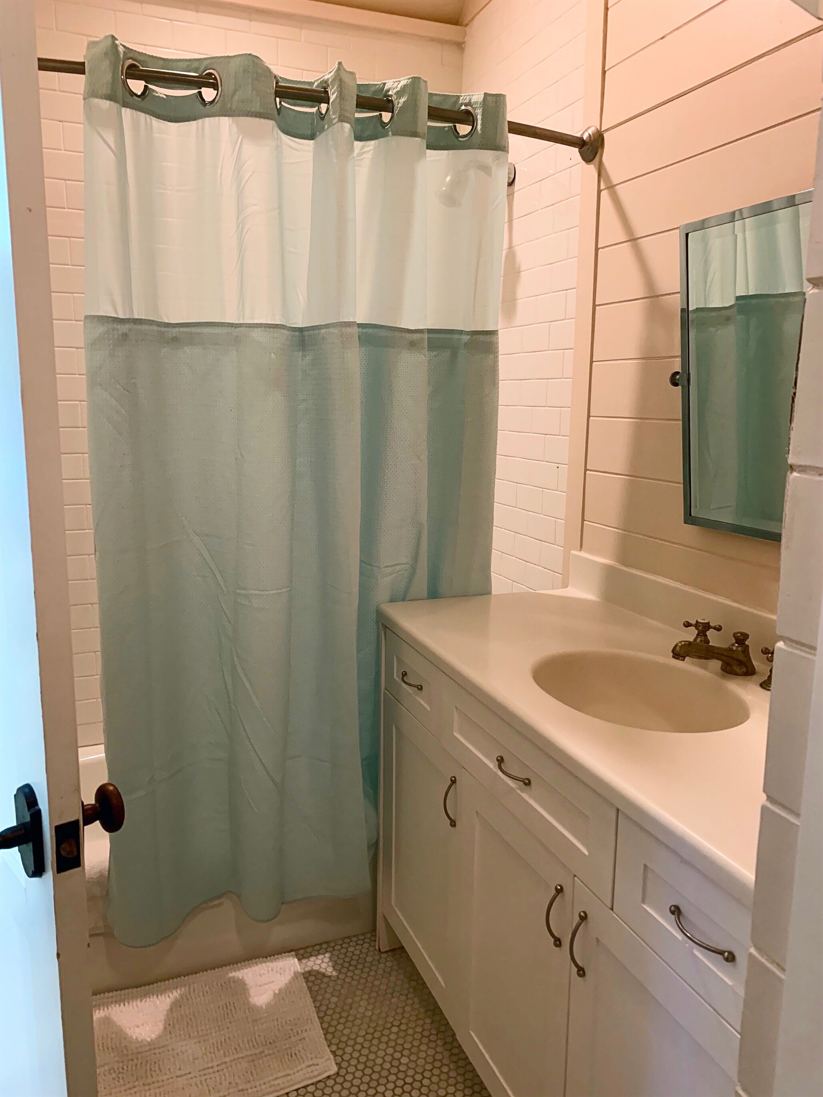 A bathroom with a shower curtain, a sink, and a mirror.