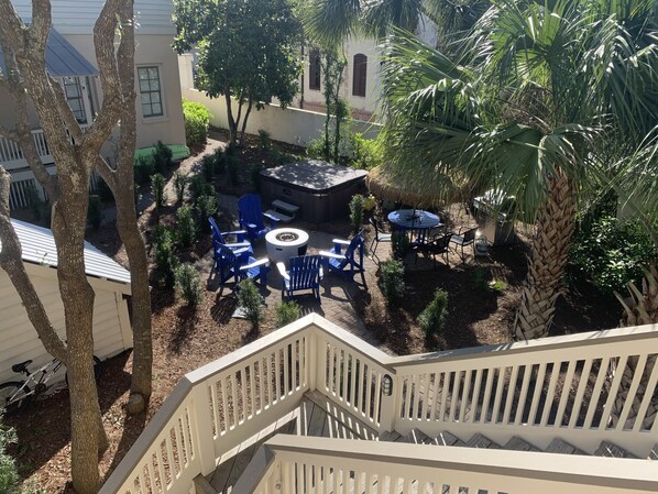 A patio area with a round table and blue chairs, surrounded by various plants and a palm tree.