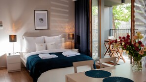 Een hotelkamer met een bed, nachtkastjes, een bureau, stoelen, een eettafel en uitzicht op het landschap.