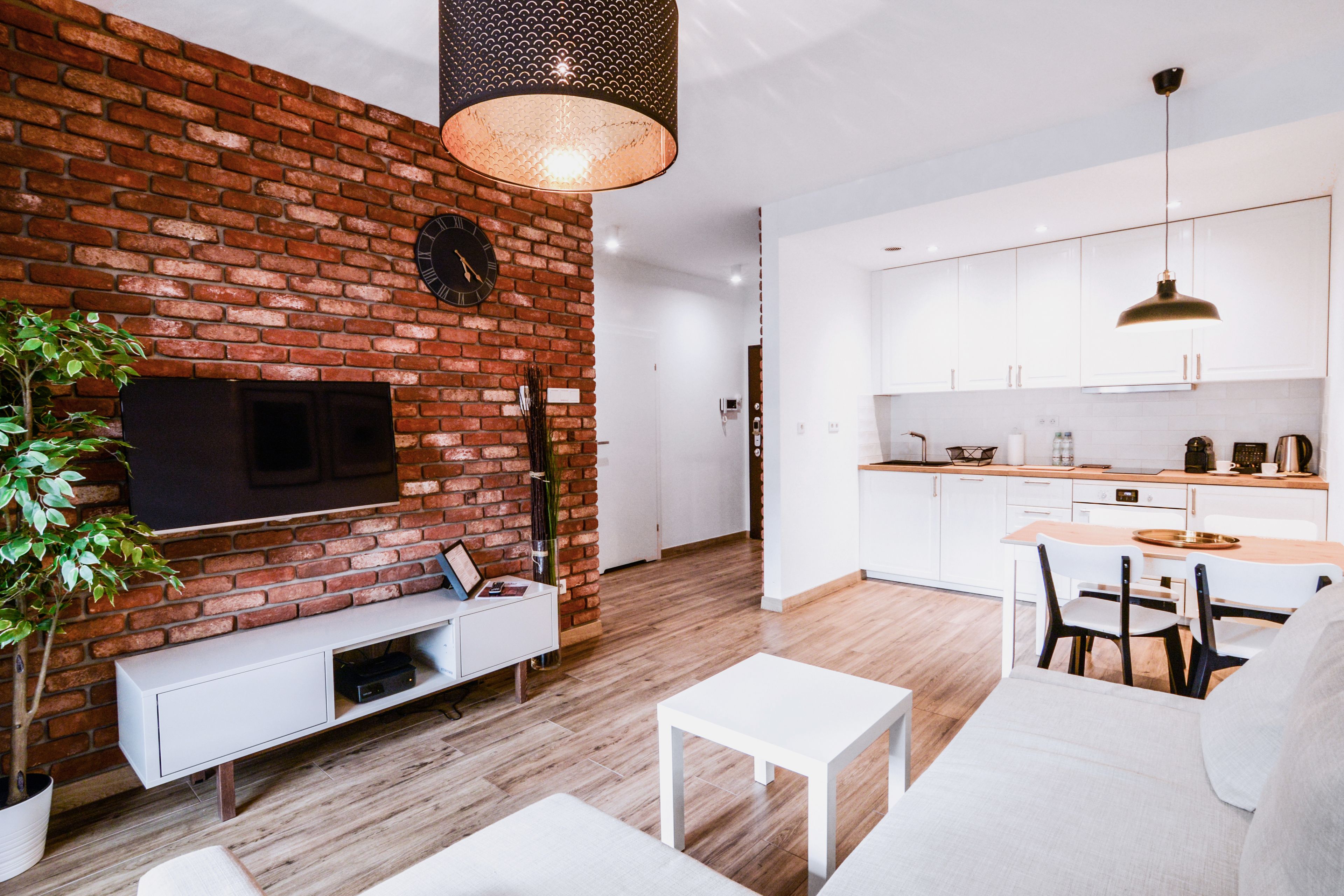 Uma sala de estar moderna com parede de tijolos, televisão de tela plana, sofá branco, mesa de centro e área de jantar com mesa e cadeiras de madeira.