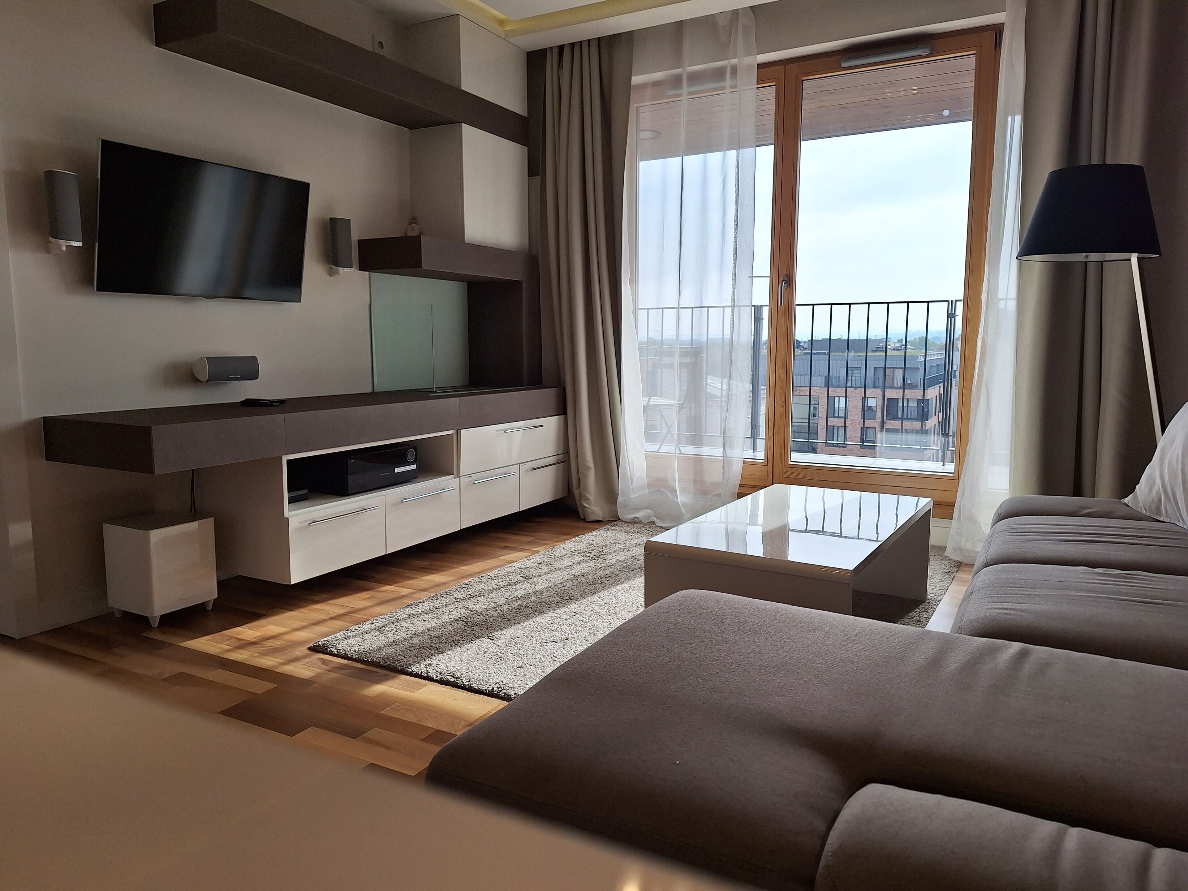 Una sala de estar moderna con un televisor de pantalla plana, mueble empotrado para entretenimiento, un sofá y un ventanal con vistas a edificios.