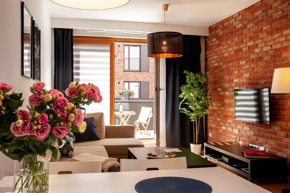 Una sala moderna con pared de ladrillo, un televisor de pantalla plana, una zona de comedor con mesa y sillas, y un sofá.