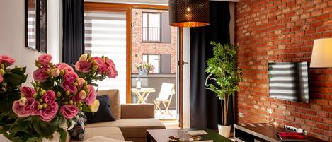 A modern living room with a brick wall, a flat-screen TV, a dining area with a table and chairs, and a sofa.